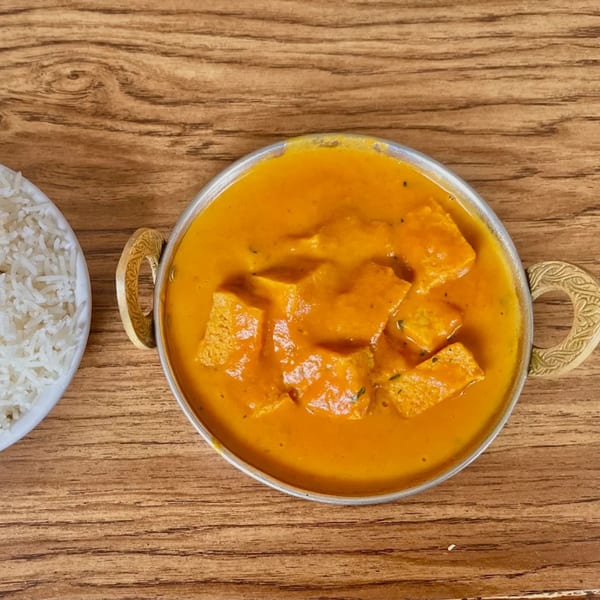 Indian paneer butter masala in a brass bowl with a side of white rice on a wooden table.