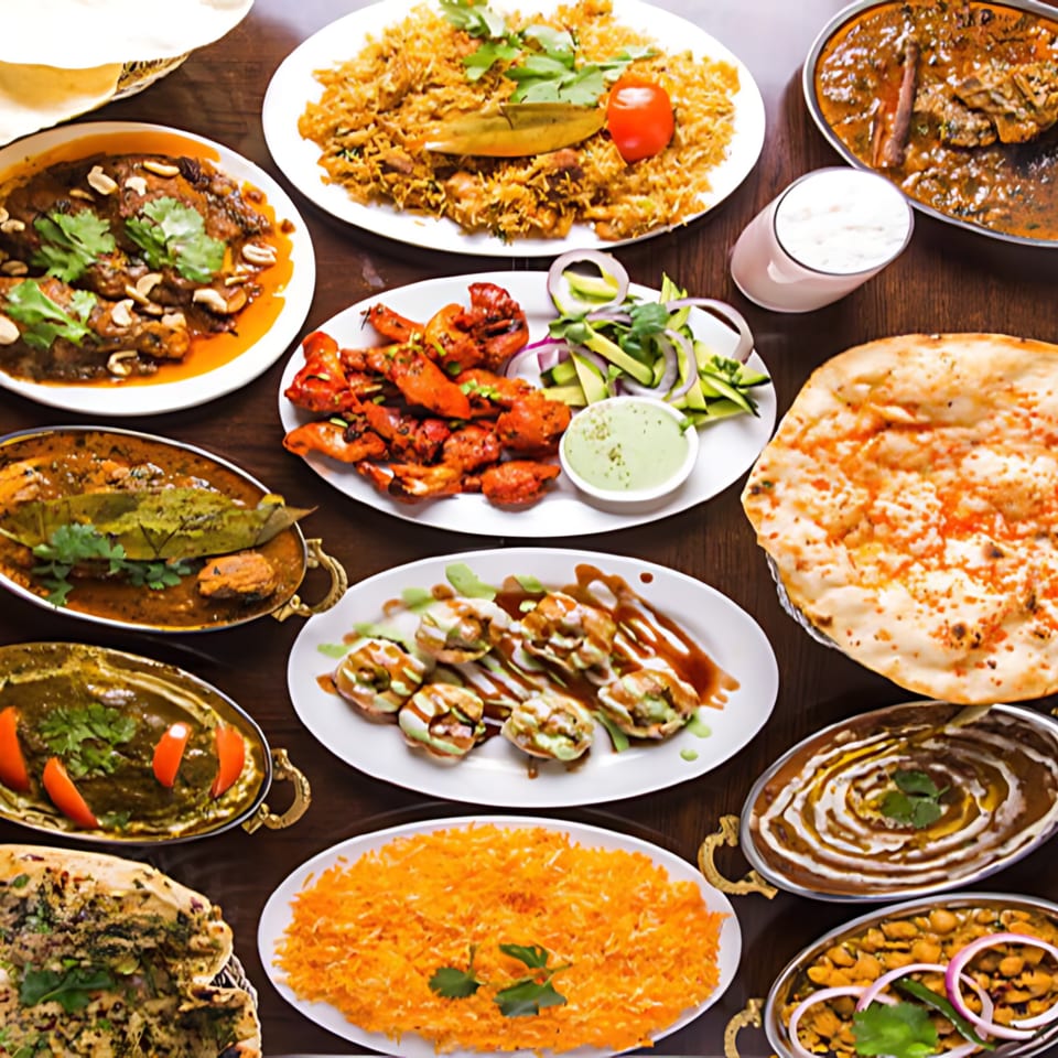 A vibrant spread of Indian dishes, including curries, rice, naan, and appetizers, on a wooden table.