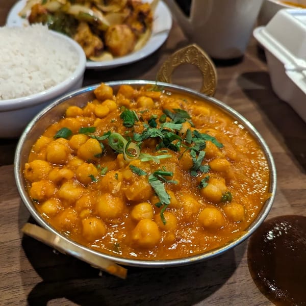A close-up of a bowl of chana masala, garnished with cilantro, next to a bowl of white rice.