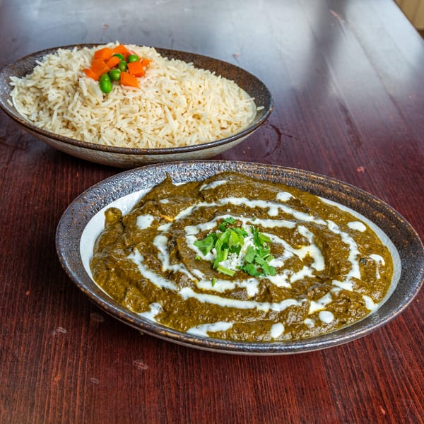 Indian palak paneer with cream swirls and cilantro, served with a bowl of rice and vegetables.