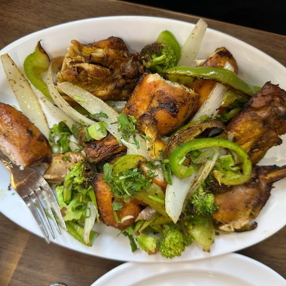 Indian grilled chicken with bell peppers, onions, and broccoli on a white plate with a fork.