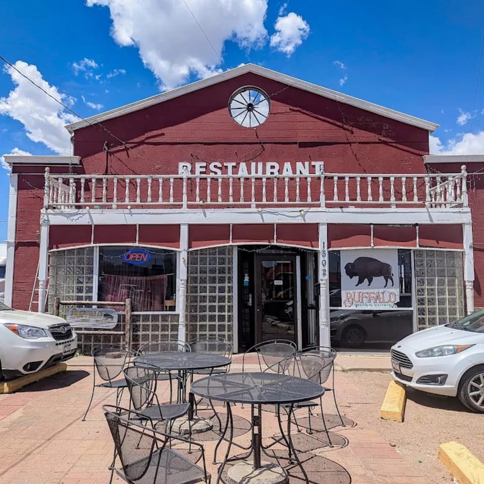 The red facade of Buffalo Indian Restaurant with outdoor seating and cars parked in front.