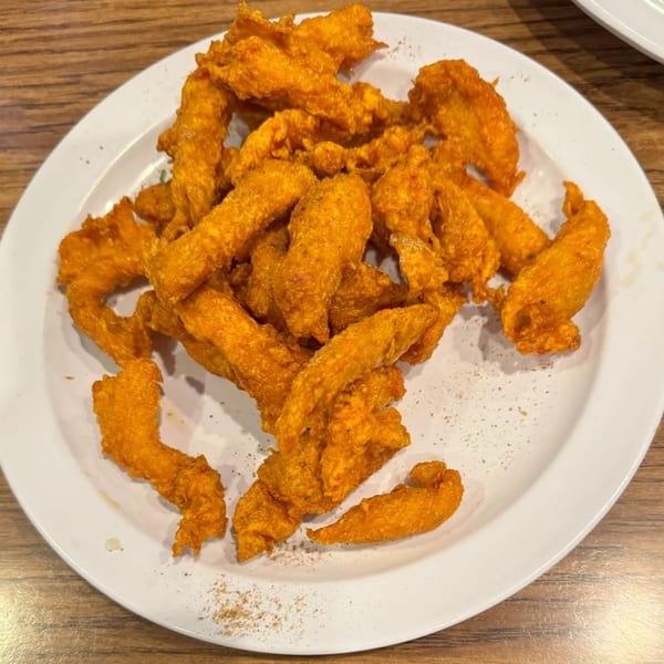 A white plate filled with golden-brown, crispy Indian chicken pakora on a wooden table.