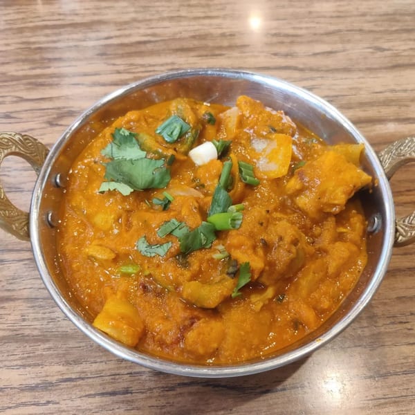 Indian curry in a metal serving bowl, garnished with fresh cilantro and green onions.