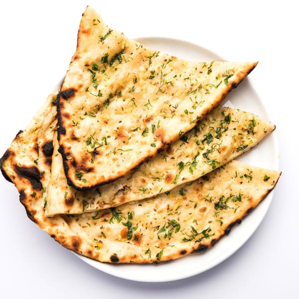 A white plate holds several pieces of golden-brown Indian naan bread, garnished with green herbs.
