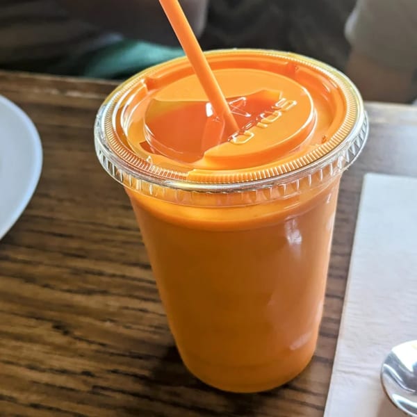 Orange drink in a clear plastic cup with a straw on a wooden table.