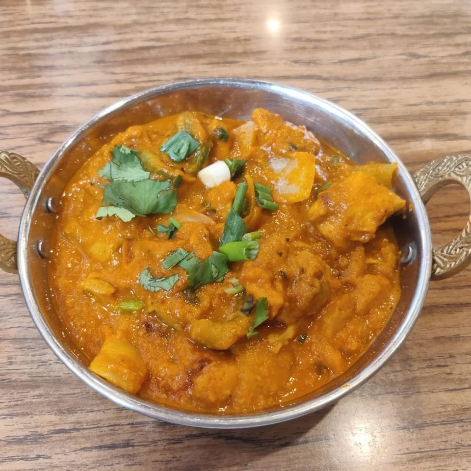 Indian curry with paneer, green peppers, and cilantro in a metal bowl on a wooden table.