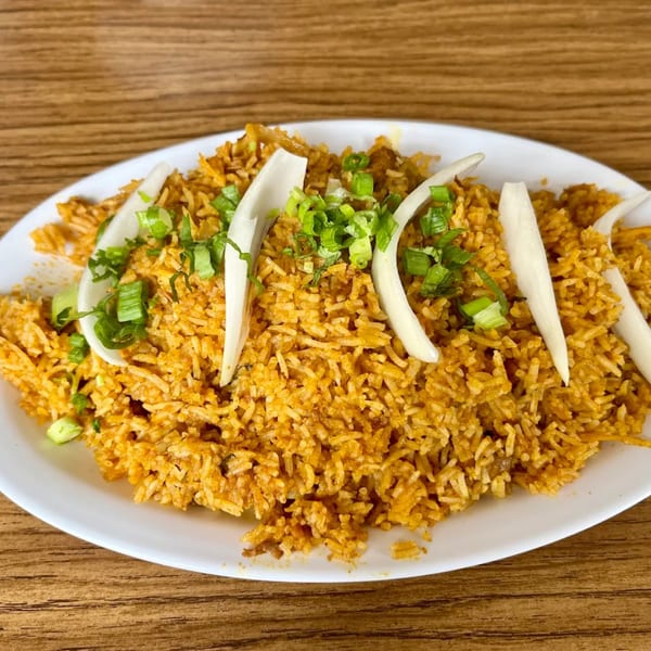 A plate of Indian biryani rice, garnished with sliced onions and chopped green onions, on a wooden table.