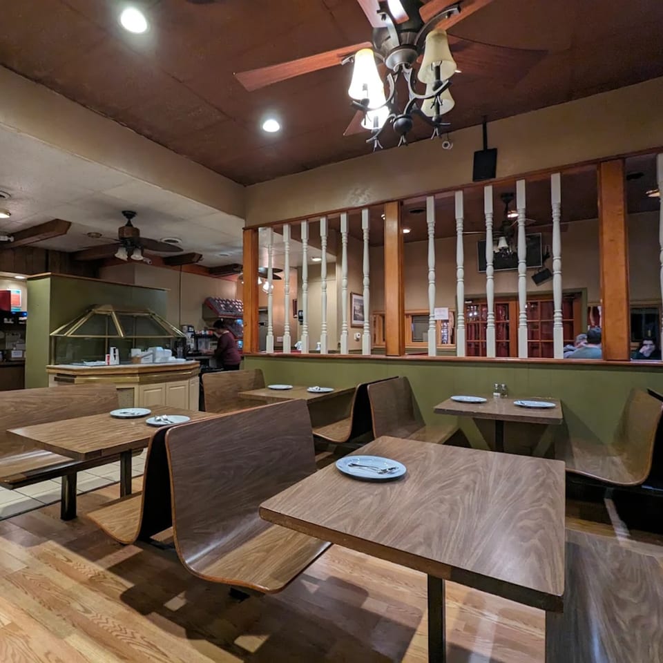 Interior of Buffalo Indian Restaurant with empty wooden tables and booths, a buffet counter, and a few patrons.