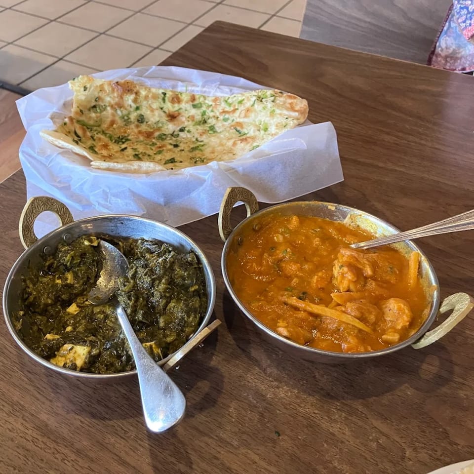 Indian dishes: Palak Paneer, Chicken Tikka Masala, and garlic naan on a wooden table.