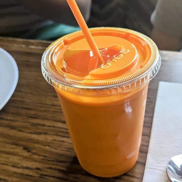 A vibrant orange drink with a straw in a clear plastic cup on a wooden table.
