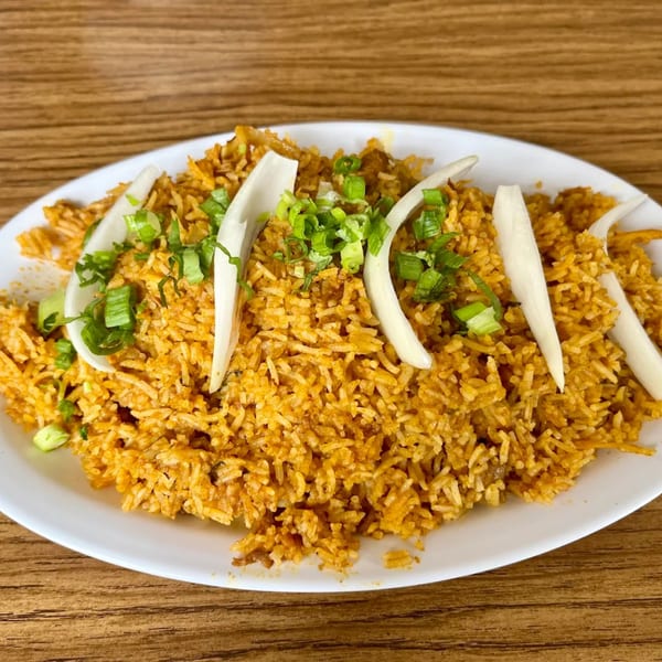 Indian biryani rice dish, garnished with sliced onions and chopped green onions on a white plate.